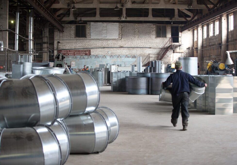 Worker in industrial warehouse with metal barrels.